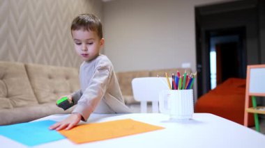 Çocuk evde yaratıyor. Bir çocuk renkli kağıtlar ve kapalı bir ortamda bir masanın üzerindeki bir araçla el sanatları üzerine odaklanır..