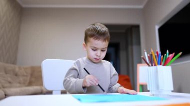 Çocuklar kapalı mekânlarda çizim yapmaya bayılır! Sanatla uğraşan küçük bir çocuk, kapalı bir ortamda bir masa kağıdını boyamaya odaklanmış..