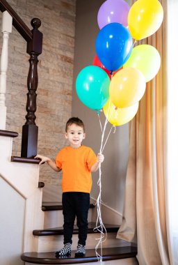 Balonlu çocuk merdivenlerde. Genç bir çocuk merdivenlerde neşeli bir şekilde duruyor. Bir sürü renkli balon tutuyor..