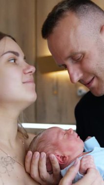 Mutlu beyaz çift öpüşmeleri. İlk kez ebeveynler yeni doğan bebeklerine sevgiyle bakıyorlar. Dikey video