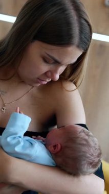 Yeni doğmuş bir bebeği elinde tutan beyaz bir anneye bayılıyorum. Annem mavi tulumlu çocuğa el sallıyor. Dikey video