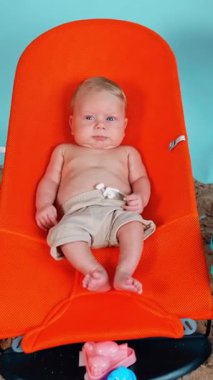 Şort giyen küçük sarışın çocuk turuncu bebek koltuğunda yatıyor. Plaj tatiline çıkmış küçük bir çocuk. Dikey video