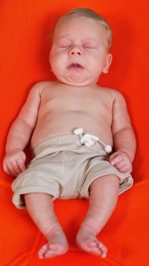 Turuncu sandalyede uzanan gevşemiş bebek. Çocuğun etrafında kum ve yüzme çemberi. Dikey video