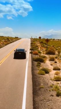 Çölde otobanın yanından geçen siyah bir arabaya yetişmek. Nevada 'daki kuru vadinin üzerinde yükselen insansız hava aracı arka planda dağlarla çevrili. Dikey video
