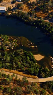 Üzerinde köprü olan güzel mavi bir göl ve otobandan geçen bir araba. Sierra Ulusal Ormanı manzarası, Kaliforniya, ABD tepeden. Dikey video