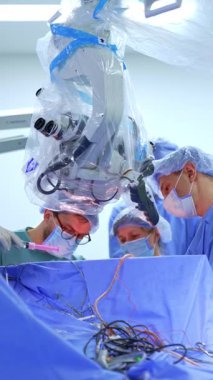 Operasyonda çalışan odaklanmış bir grup cerrah. Plastik kaplı mikroskop hastanın üzerinde. Dikey video.