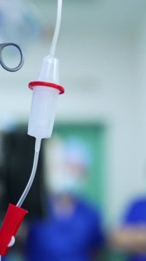 Mavi bornoz giyen kadın doktor, maske ve kapak mikroskoba bakıyor. Doktor ameliyat masasına metal bir alet koyar ve şırıngayı alır. Dikey video.