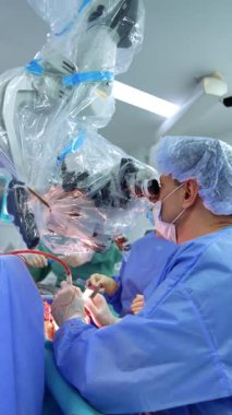 Beyaz erkek cerrah tarafından yapılan beyin cerrahisi. Doktor mikroskoba elektrikli cihaz ve metal aletlerle bakıyor. Dikey video.