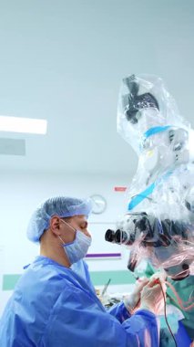 Elektrikli alet tutan beyaz cerrah mikroskobun dürbününü hareket ettiriyor. Doktor beyin cerrahisi yapar. Dikey video.