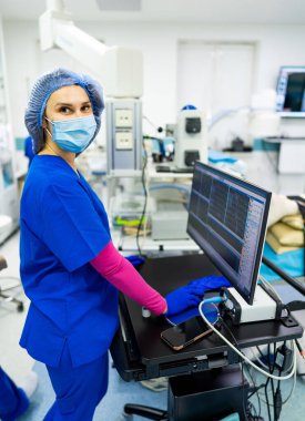 Klinik sağlık çalışanı. Mavi önlüklü tıbbi personel, klinik bir ortamda hasta bakımına hazırlanırken monitör kullanıyor..
