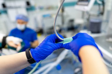 Cerrahi ekip aletleri kurar. Mavi önlüklü tıp uzmanları ameliyathanedeki hastaya odaklanırken cerrahi ekipman hazırlıyorlar..