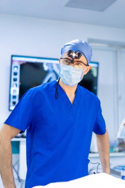 Klinikte ameliyat hazırlığı. Mavi önlüklü bir cerrah ameliyathanede duruyor, odaklanmış ve ameliyata hazır..