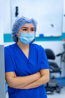 Hemşire hastalar için hazırlanır. Mavi önlüklü ve maskeli bir hemşire bir sonraki hastasıyla karşılaşmak için hastanede sakince bekliyor..