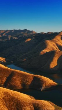 Suyun derinliklerine inen dağların büyüleyici manzarası. Kaliforniya 'da yuvarlanmış kayalardan oluşan güzel bir manzara ve onları çevreleyen bir göl. Üst Manzara. Dikey video