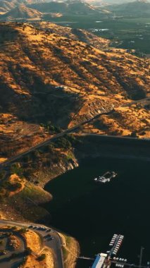 Kaliforniya dağlarında gölün üzerinde uçuyor. Arka planda güneşli yeşil vadiler. Hava perspektifinden bak. Dikey video