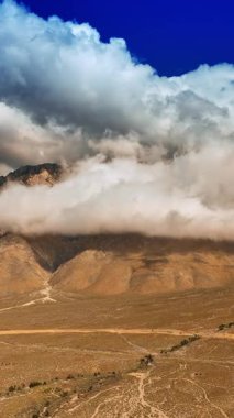 Ölüm Vadisi 'ndeki dağların tepelerini kaplayan devasa bulutlar. Etrafı kayalarla çevrili güzel bir çöl manzarası. Üst Manzara. Dikey video