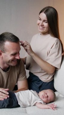 Üç kişilik mutlu bir beyaz aile. Kadın kocasının saçlarını, uyuyan bebeğin üzerinde otururken tarıyor ve sonra da çocuğun saçını tarıyor. Dikey video