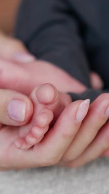 Kahverengi kol saati olan bir kadın el küçük bebek ayak parmaklarını okşar. Annesinin ellerinde şirin bebek ayakları var. Kapatın. Dikey video