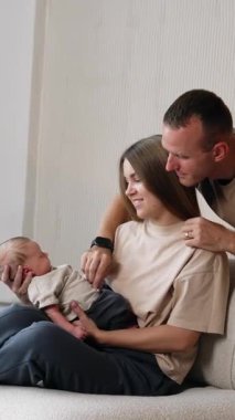 Mutlu aile fotoğrafı. Bej tişörtlü ebeveynler bebeklerinin annesinin ellerinde huzurlu bir şekilde uyuduğunu görüyorlar. Dikey video