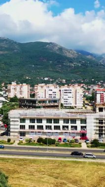 Karadağ 'ın Bar kentindeki apartman ve otoyol bloklarının üzerinde uçuyor. Arkaplanda beyaz bulutlu yeşil dağlar. Hava görüntüsü. Dikey video