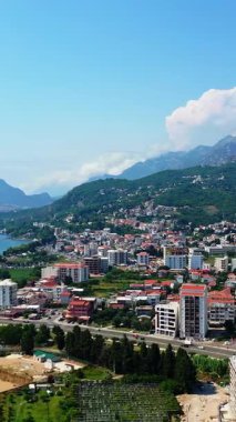 Karadağ 'daki yeşil dağların yamaçlarında yer alan güzel bir şehir barı. Göz kamaştırıcı doğanın arka planında güneşli şehir manzarası. Havadan bakış açısı. Dikey video