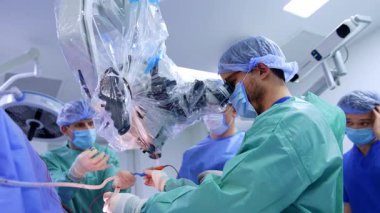 Sakallı cerrah, mikroskop olmadan asistanından alet alır. Nöroşirürji yapan doktora düşük açılı bakış açısı.