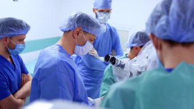 Modern ameliyat odasındaki ameliyat masasında büyük bir grup doktor var. Tıbbi ekip ameliyatta kullanmak için mikroskop hazırlıyor..