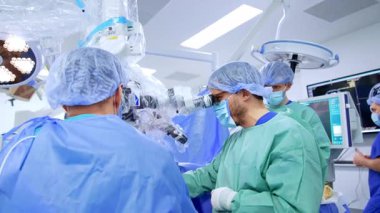 Sakallı beyaz cerrah mikroskoba bakar. Sağlık ekibi beyin cerrahisinde işbirliği yapıyor..