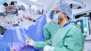 Erkek doktorun elinde cerrahi bir sonda var. Beyin cerrahı hastanın beynine sonda yerleştirir ve mikroskoba bakar..