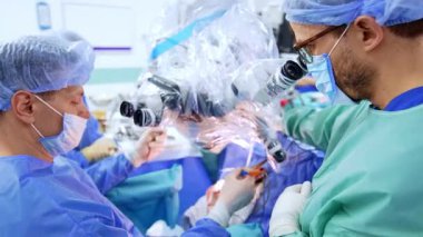 Ameliyatta iki erkek cerrah konuşuyor. Beyin cerrahı mikroskobu plastikle kaplıyor..