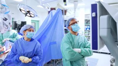 Cerrahlar monitörün konuşmasına bakar. Ameliyat masasında oturan beyin cerrahı kullanılmış aracı asistana geçirir.