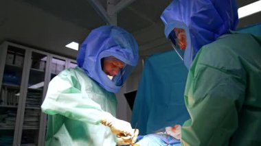 Ortopedik cerrahlar travma geçirmiş bacakları ameliyat ederler. Koruyucu kask takan erkek cerrahlar ameliyat yaparlar..