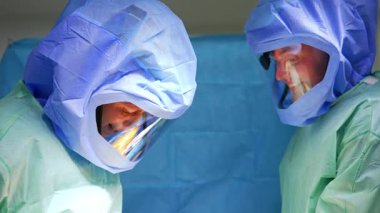 Koruyucu kask takmış gülümseyen beyaz erkek cerrahlar ameliyatta işbirliği yapıyor. Doktorlar travmayı ameliyat ediyorlar..