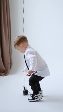 Beyaz gömlek giyen, siyah kot pantolon giyen ve güneş gözlüğü tutan sevimli bir bebek. Çocuk neşeli bir şekilde bir balonla oynuyor. Dikey video.