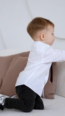 Küçük çocuk kanepede neşeyle koşuyor. Kafkas bebek balonlarla oynuyor. Dikey video.