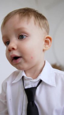 Beyaz gömlekli, siyah kravatlı, kızıl saçlı, beyaz bir bebek. Meraklı küçük bir çocuğun portresi. Kapatın. Dikey video.