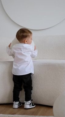 İki yaşında küçük bir çocuk kanepeden büyük bir yuvarlak yastık alır ve onu yere bırakır. Küçük çocuk kameraya yaklaştı. Dikey video.