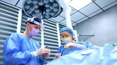 Erkek doktor ve kadın ameliyat hemşiresi hastanede estetik ameliyat yapıyor. Cerrah metal alet ve cihaz kullanır ve hemşire doktora yardım eden aleti destekler. Düşük açı görünümü.
