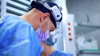 Koyu mavi şapkalı erkek doktor, maske, hastanın üzerine eğilen cerrahi hoparlörler. Profesyonel cerrah metal aletler kullanır. Ameliyat hemşiresi asistanı..