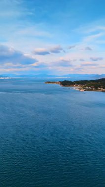 Mavi Japon İç Denizi 'nin su yüzeyinde birkaç tekne var. Suyun üstündeki insansız hava aracı görüntüleri Itsukushima Tapınağı ile Japonya Miyajima 'nın manzarasını gözler önüne seriyor. Dikey video.