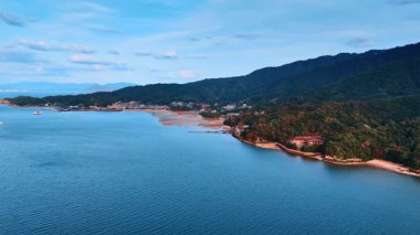 Sakin mavi suların üzerinden uçarak alçak gelgit mevsiminde Itsukushima Tapınağı 'nın ünlü kırmızı kapılarına yaklaşıyorlar. Japon İç Denizi kıyısındaki ağaçlarla kaplı dağların muhteşem manzarası..