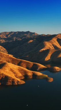 Çıplak bir dağın eteğindeki su deposu. Su ve çöl karışımı. Kaliforniya çölünün güzel manzarası tepeden. Dikey video