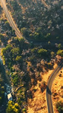 Kaliforniya dağlarında tehlikeli bir otoyol. Nehrin üzerindeki yol kayaların arasında akıyor. Üst Manzara. Dikey video