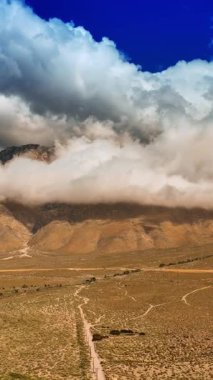Dağların tepelerini gizleyen beyaz bulutlar. Kayaların dibindeki terk edilmiş topraklar. Ölüm Vadisi 'ne hava perspektifi. Dikey video