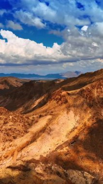 Mojave Çölü 'nün inanılmaz çıplak kayaları. İnsansız hava aracı, beyaz bulutlarla gölgelenmiş dağların tepelerine yaklaşıyor. Dikey video
