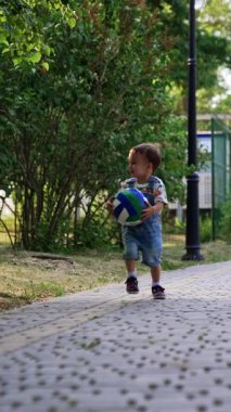 Sevimli mutlu çocuk top taşıyan bir topla koşuyor. Bebek yazın parkta iyi vakit geçiriyor. Dikey video