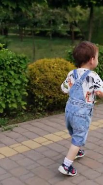 Yolda koşan kot pantolonlu bir çocuğu takip ediyormuş. Yaz parkında yürüyüş yapan mutlu bir bebek. Dikey video