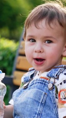 Güzel bebek bankta oturuyor. Kameraya konuşan bir çocuğun portresi. Dikey video