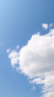 Açık mavi yaz gökyüzü ara sıra beyaz bulutlar beliriyor ve şekil değiştiriyor. Bulutların üzerinde parlayan parlak güneş. Düşük açılı zaman dilimi. Dikey video