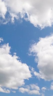 Kabarık bulutlu mavi yaz gökyüzü. Atmosferde beyaz bulutlar görünür ve kaybolur. Düşük açı. Zaman ayarlı. Dikey video